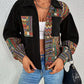 Person wearing a black jacket with colorful patterned sleeves and a white top, standing against a plain background.