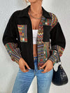 Person wearing a black jacket with colorful patterned sleeves and a white top, standing against a plain background.