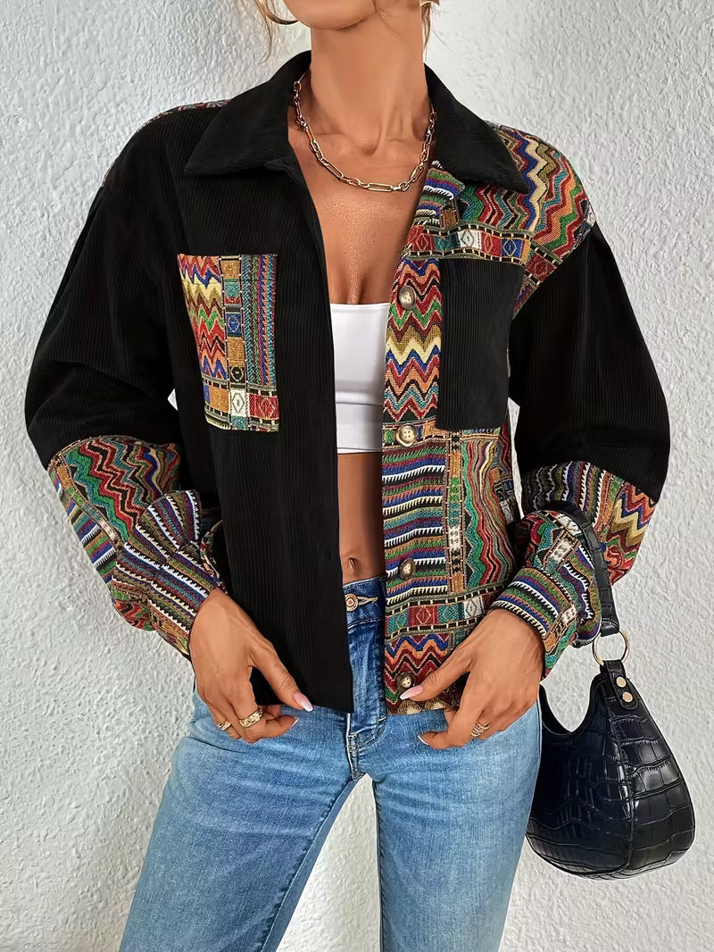 Person wearing a black jacket with colorful patterned sleeves and a white top, standing against a plain background.