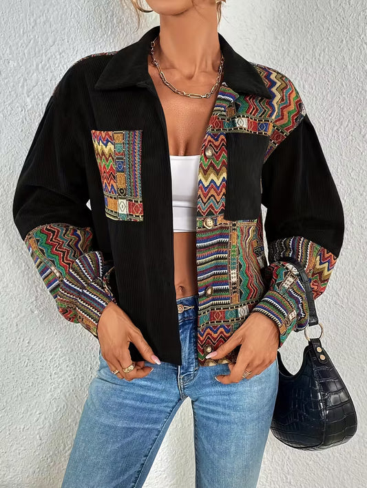 Person wearing a black jacket with colorful patterned sleeves and a white top, standing against a plain background.