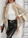 Person wearing a beige knitted shawl with fringe, white sweater, black leather pants, and holding a clutch.