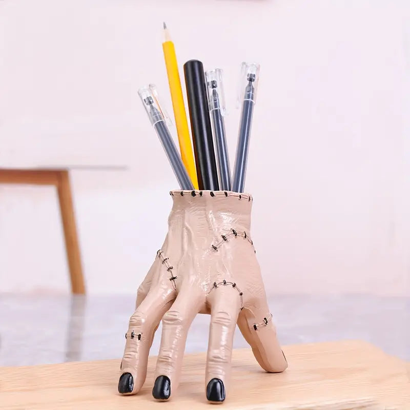 Pencil holder shaped like a hand with black nail polish holding pens on a wooden surface.