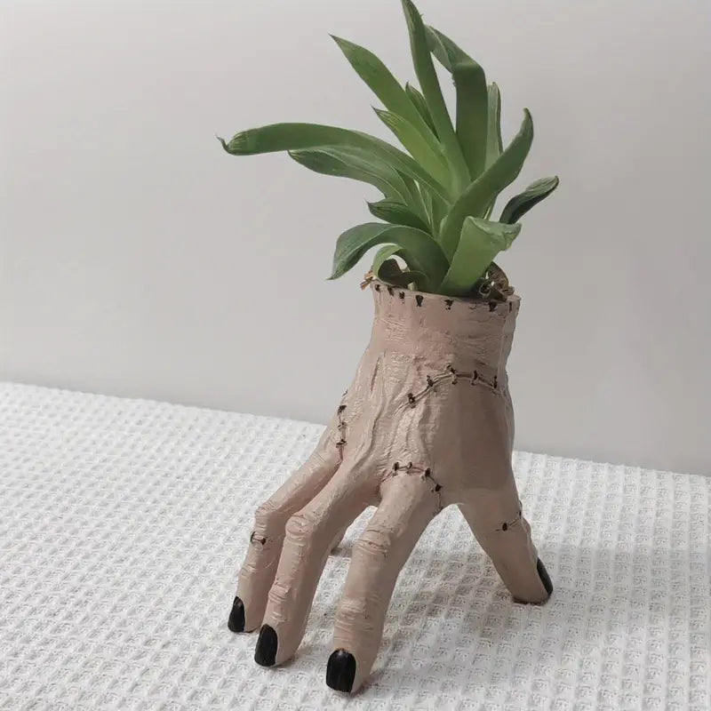 Hand-shaped plant pot with a green plant on a textured surface